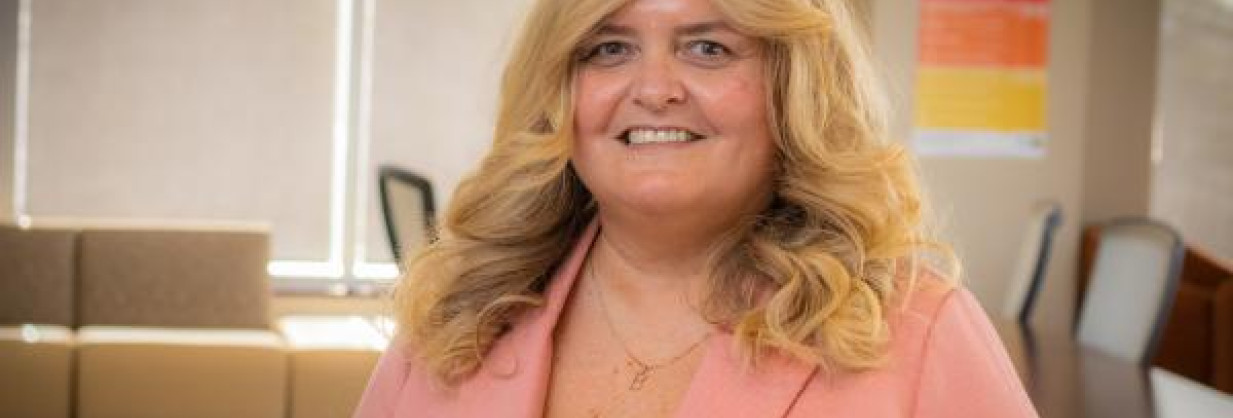 smiling blonde physician leader wearing pink jacket in a boardroom