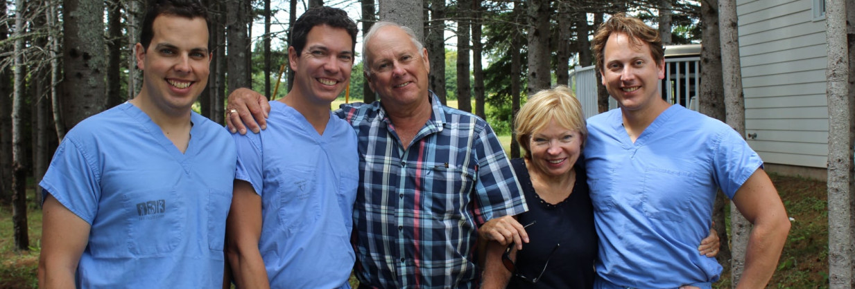 Three smiling young physicians in blue scrubs standing with mom and dad