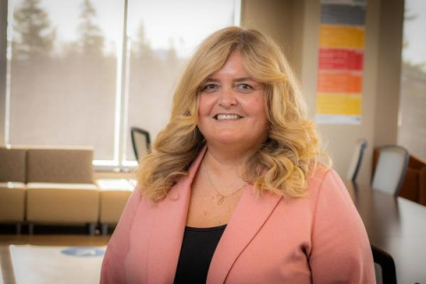 smiling blonde physician leader wearing pink jacket in a boardroom