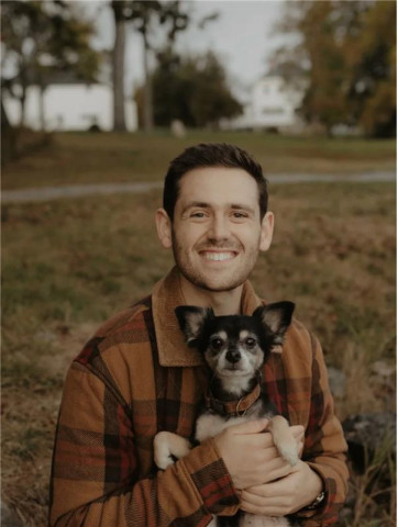 Man with brown hair is holding a black and white dog.