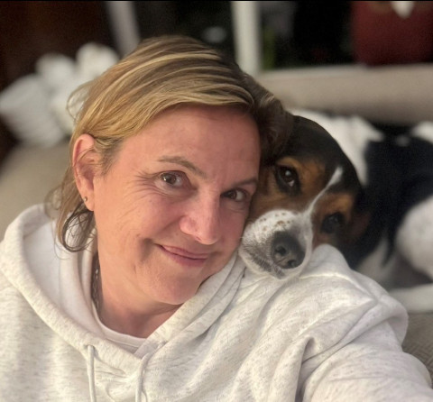 Woman with her dog. She has blonde hair and is wearing a white sweater. Her dog is black, brown and white on the face. 