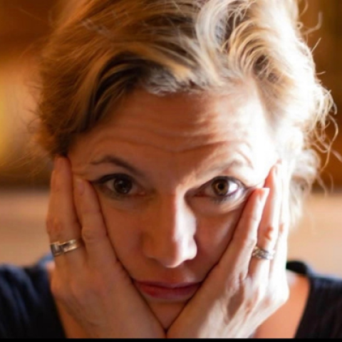 Woman with blonde hair. Her hands are on either side of her face
