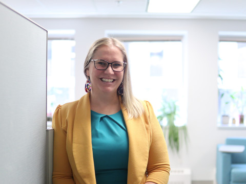 young woman with long blonde hair and glasses with friendly smile and mustard blazer