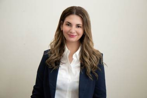 headshot with long brown curly hair. Wearing a black blazer over a white buttoned top