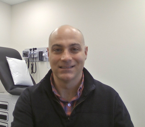 a man with black zip up sweater over a plaid red and blue shirt.