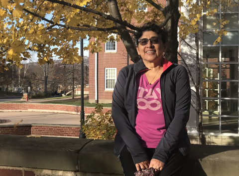 Smiling doctor seated outside wearing jacket and pink sweater