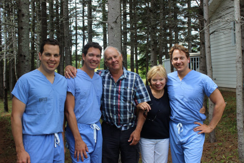 Three smiling young physicians in blue scrubs standing with mom and dad