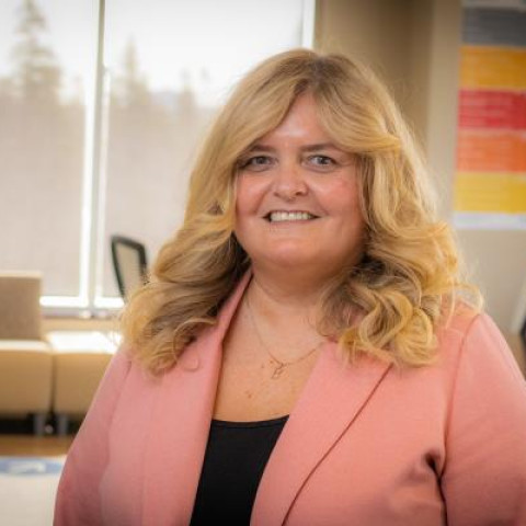 smiling blonde physician leader wearing pink jacket in a boardroom