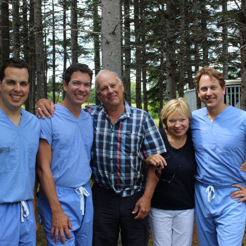 Three smiling young physicians in blue scrubs standing with mom and dad